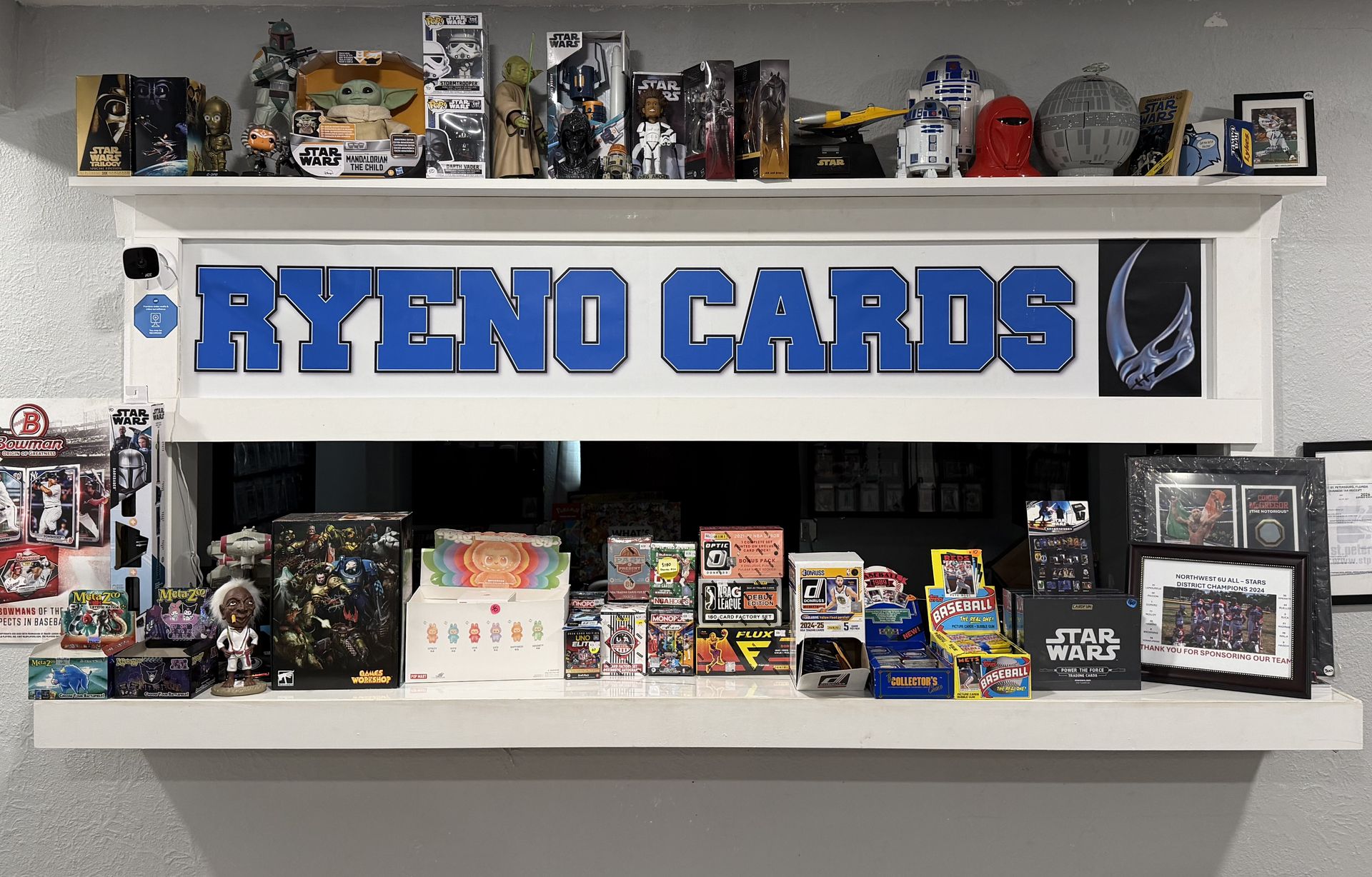 The Ryeno Cards counter: the shop sign in blue block letters, Star Wars figures on the shelf above and sealed boxes below